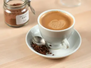 Kubek spienionego hojicha latte z liśćmi herbaty i łyżeczką, ilustrujący prosty przepis na przygotowanie napoju